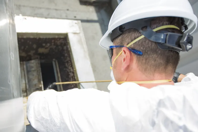 Technician in a hard hat working at an opened exhaust duct access hatch